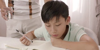 亚洲父亲站着，听着沮丧的儿子模糊地写作业