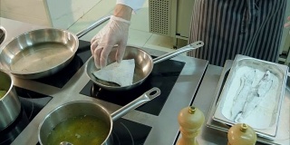 厨师把撒了面粉的鱼放在煎锅里，另一个厨师在做土豆泥