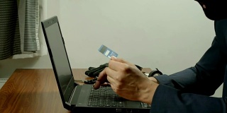 一个穿着西装的蒙面罪犯拿着伪造的信用卡在网上进行诈骗。