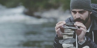 一个年轻人在河边用石头筑塔。寻找平衡