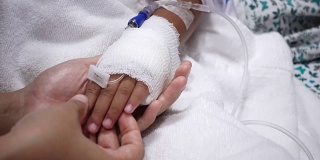 年轻的父母和生病的小女儿抱着绷带的手舒适在医院的床上