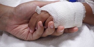年轻的父母和生病的小女儿抱着绷带的手舒适在医院的床上