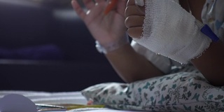 特写的童年包扎的手与颜料彩色铅笔在一张纸上医院。治疗室实时拍摄。年轻病人的放松时间。