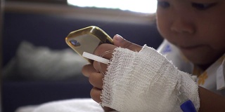 婴儿女儿在病床上使用智能手机的特写。年轻病人的放松时间。治疗室实时拍摄。