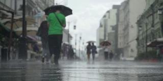 背景大雨天在城市街道。真正的时间。人们在雨中带着雨伞上下班。年轻女孩拿着五颜六色的雨伞。模糊的散景。自然背景