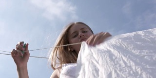 蓝天下，一个年轻的女孩在晾衣绳上挂着白色的床单