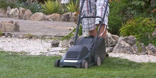 在花园工作的房主使用割草机修剪草坪