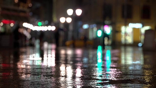 抽象明亮模糊的背景与雨滴，沥青照明路灯和交通灯。身份不明的女孩在雨夜的城市街道上。商店橱窗和街灯在潮湿的路面上发出明亮的照明和反射