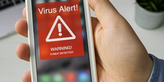 一名男子手持智能手机，屏幕上显示着病毒警告信号