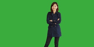 穿着蓝色外套的年轻亚洲女人。使用智能手机，数字平板电脑和看相机。一个站在绿屏前的女人。