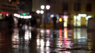 抽象明亮模糊的背景与雨滴，沥青照明路灯和交通灯。身份不明的女孩在雨夜的城市街道上。商店橱窗和街灯在潮湿的路面上发出明亮的照明和反射视频素材模板下载
