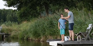 时髦的爸爸和男孩在池塘边钓鱼