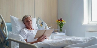 愉快的老住院病人在床上看书