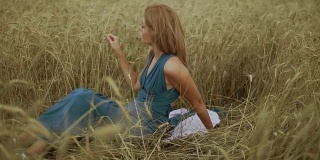 迷人的年轻女子坐在金色的麦田里。她的手正在摸麦穗。收获的概念。收割。慢动作镜头