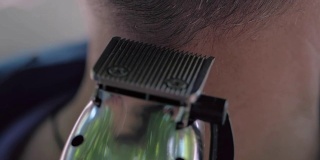 理发师在给一个男人理发。一位中年妇女理发师用机器为一位灰白头发的黑发男子理发。夏天在户外理发。特写,慢动作