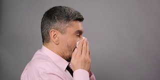 鼻炎,过敏病。患病男性打喷嚏并用纸巾擦鼻子