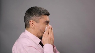 鼻炎,过敏病。患病男性打喷嚏并用纸巾擦鼻子视频素材模板下载