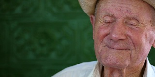 很有感情的老人肖像。爷爷开心地笑着。人像:年事已高，年事已高。一个沉思的老人在夏天独自坐在户外白色帽子的特写。慢动作