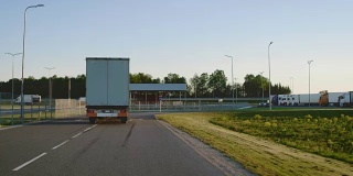 半卡车与货运拖车在高速公路上左转的后续镜头。卡车移至卸货仓库区域。
