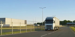 在高速公路上行驶的带有货物拖车的半卡车。白色卡车通过工业仓库区域运送货物。
