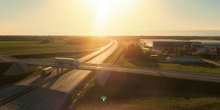 带货运拖车的白色半挂车通过高速公路立交桥鸟瞰图。十八惠勒是新的，装载仓库在背景中看到。