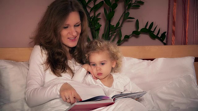 漂亮的年轻妈妈给她可爱的蹒跚学步的女儿读书
