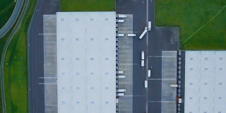 放大航拍工业仓库/仓库大楼/装卸区，许多卡车在装卸区装卸货物。