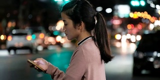 SEA:手机使用，迷人的亚洲女人在夜间城镇的街道上行走时使用手机