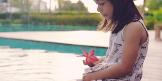 一个小女孩坐在池边，脚浸在水里，