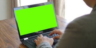商人用绿色屏幕的笔记本电脑键盘打字，摄影车从右向左拍摄