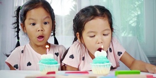 两个亚洲小女孩在家里一起吹灭生日蛋糕上的蜡烛。慢动作拍摄在工作室。