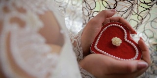 美丽女人的手捧着心形的订婚戒指盒。新娘手里拿着一个心形的礼盒