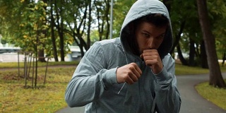 年轻的拳击手在灰色钩跑在公园和挥舞的手像拳击手