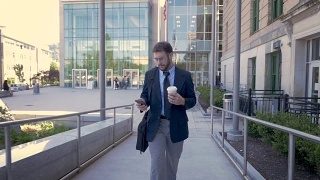 英俊的商人用手机从办公楼里走出来视频素材模板下载