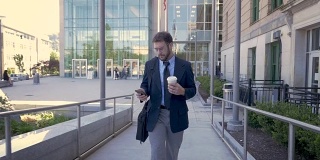 英俊的商人用手机从办公楼里走出来