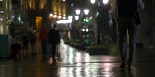 在雨夜的城市里，街道上挂满了路灯，柏油从雨中闪闪发光。不认识的行人，年轻人。现代都市夜生活的概念生活方式。汽车和行人