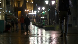 在雨夜的城市里，街道上挂满了路灯，柏油从雨中闪闪发光。不认识的行人，年轻人。现代都市夜生活的概念生活方式。汽车和行人视频素材模板下载