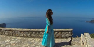 美丽的黑发微笑女孩与健康的长发在吹连衣裙。快乐的年轻女子享受和有乐趣的海洋和蓝天。Sveti Stefan、黑山