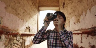 一个年轻的女人拿着一个旧相机穿过一个旧拱门拍照