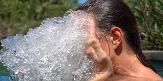 慢镜头:女孩在丛林中的游泳池里用水泼脸