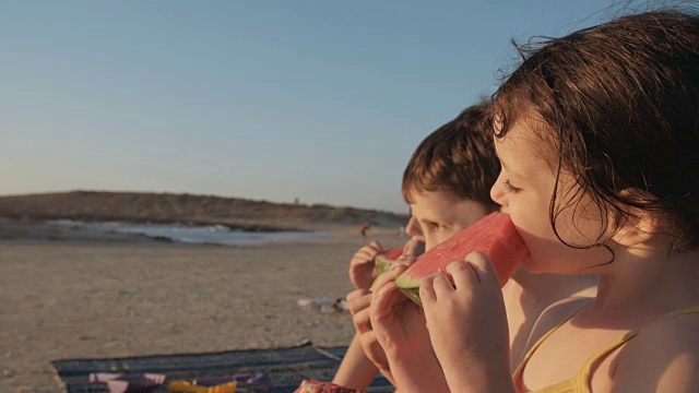 三个孩子在海滩上吃西瓜