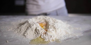 特写镜头:鸡蛋掉进厨房桌上的面粉里。Slowmotion拍摄