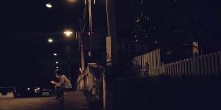 年轻的亚洲男人晚上坐着玩智能手机。