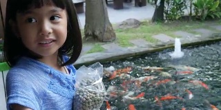 亚洲女孩在池塘里喂鲤鱼