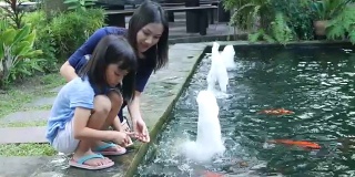亚洲女孩和母亲在池塘里喂鲤鱼