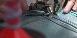 女性双手在缝纫机上把拉链整齐地缝到皮片上。概念生产皮具
