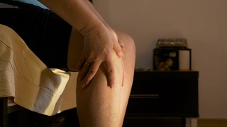 一位成年妇女坐在卧室里揉着她得了关节炎的膝盖视频素材模板下载