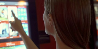 穿着红t恤的年轻漂亮女人在电影院的自动贩卖机里买电影票
