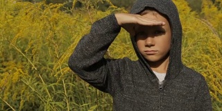 一个男孩在高高的草丛里，穿着灰色的毛衣，头上戴着兜帽