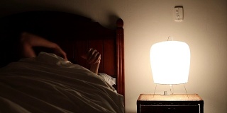 人在半夜醒来，无法入睡，患了失眠。年轻人从床头柜上打开灯，下了床